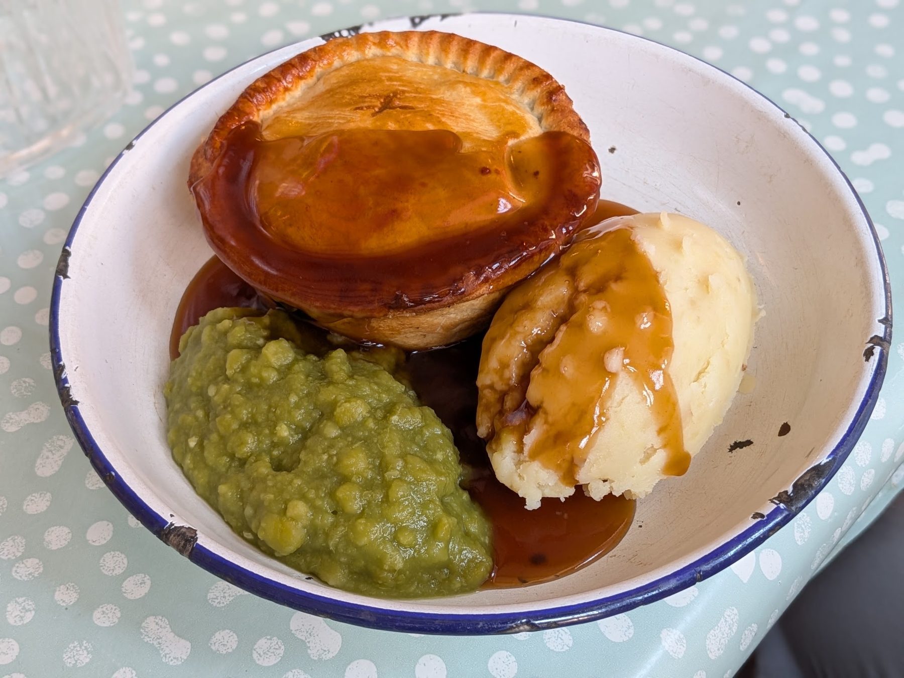 A pie with mash, mushy peas and gravy in an enamel dish