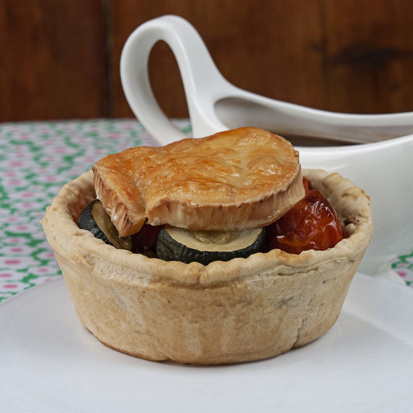 A pie in a pastry case with a gravy boat behind
